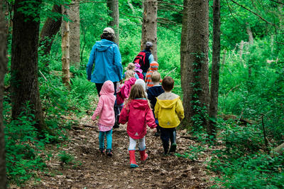 Young children with an educator walking away from the camera into the forest on a trail