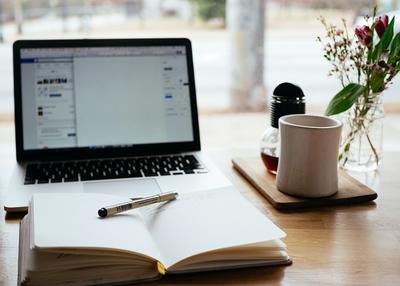 Laptop in front of an open notebook and a tea mug on a desk