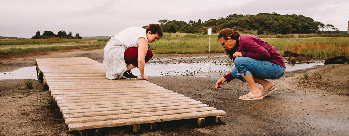 Two people investigating mud in a salt marsh at low tide