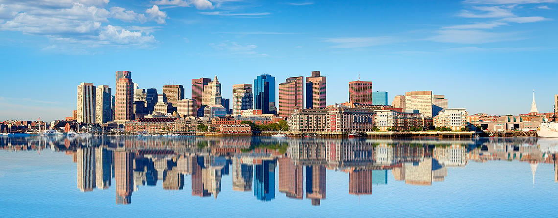 Boston city skyline reflected in calm harbor waters on a sunny summer day