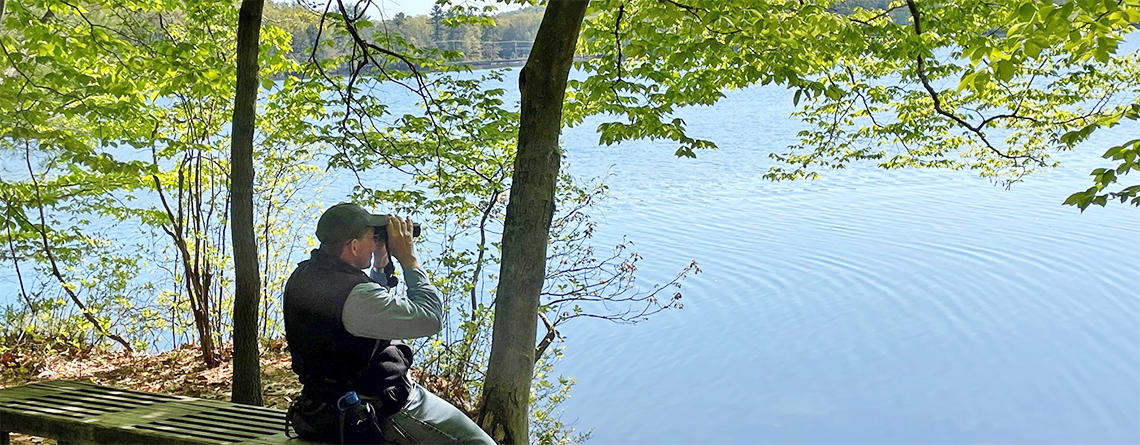 Person with binoculars looking out over the lake from Osgood Hill