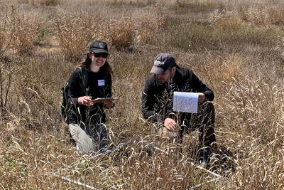 Two educators kneeling in a grassy field