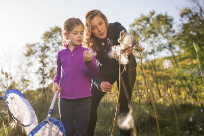 A Mass Audubon educator and a young girl examine a milkweed seed pod at Wachusett Meadow
