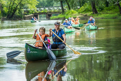 Children and adults paddling a tranquil river in canoes