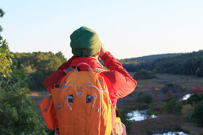 A fall hiker using binoculars to take in the view at Tidmarsh Wildlife Sanctuary
