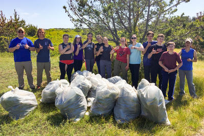 Teens standing proudly behind a pile of trash bags after cleaning up a natural area