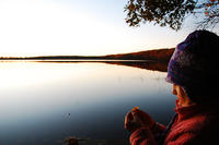 Young girl in winter gear examines a leaf by the edge of a lake © Paul Blankman