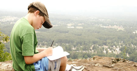 Boy journaling on a hilltop