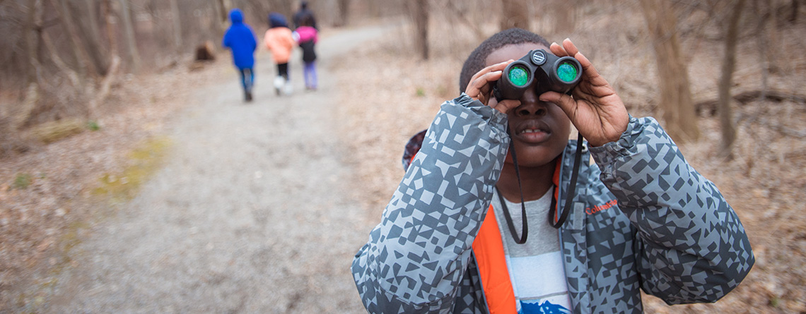 Boy looking through binoculars on a winter trail at the Boston Nature Center