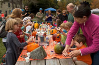 Group of adults helping children decorate pumpkins at a picnic table