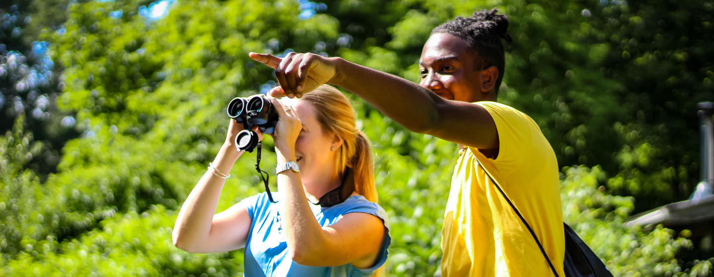Two people birding - one is looking through binoculars, one is pointing at something in the distance