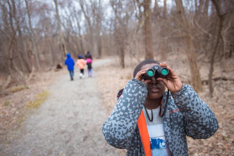 Boy looking through binoculars on a trail at Boston Nature Center in early winter