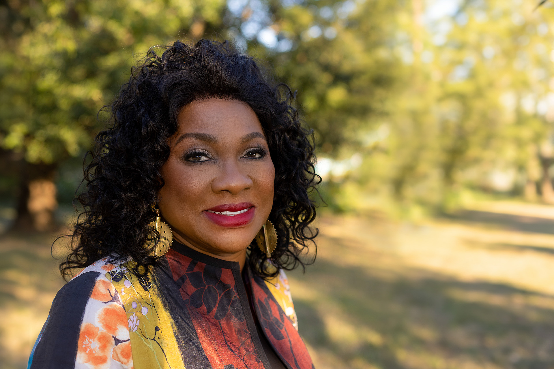 A headshot of Dr. Beverly Wright smiling and standing in front of a green, sunny forest