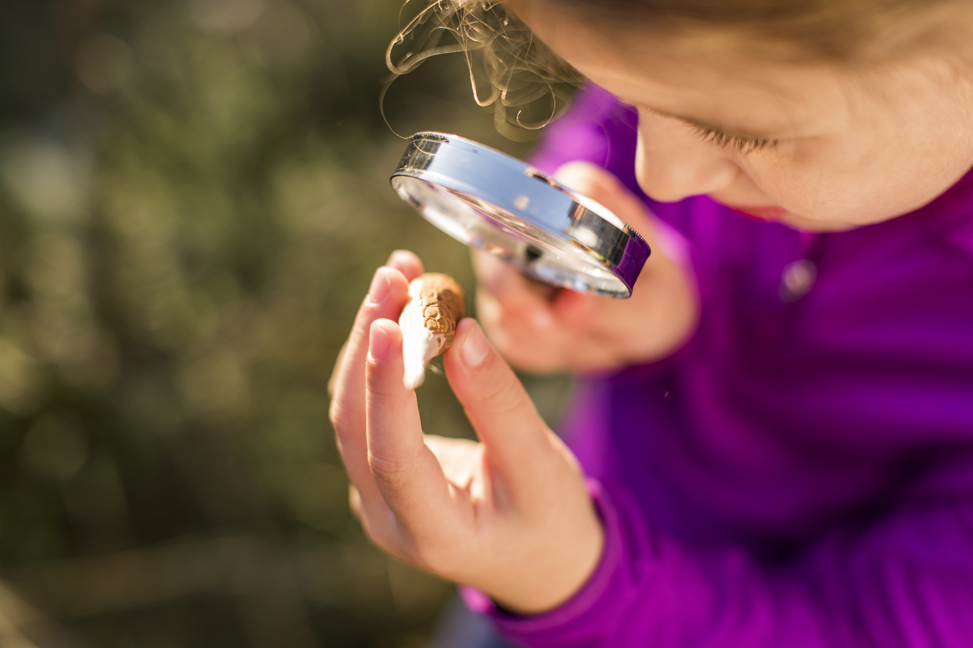 child looking through a magnifying glass at milkweed