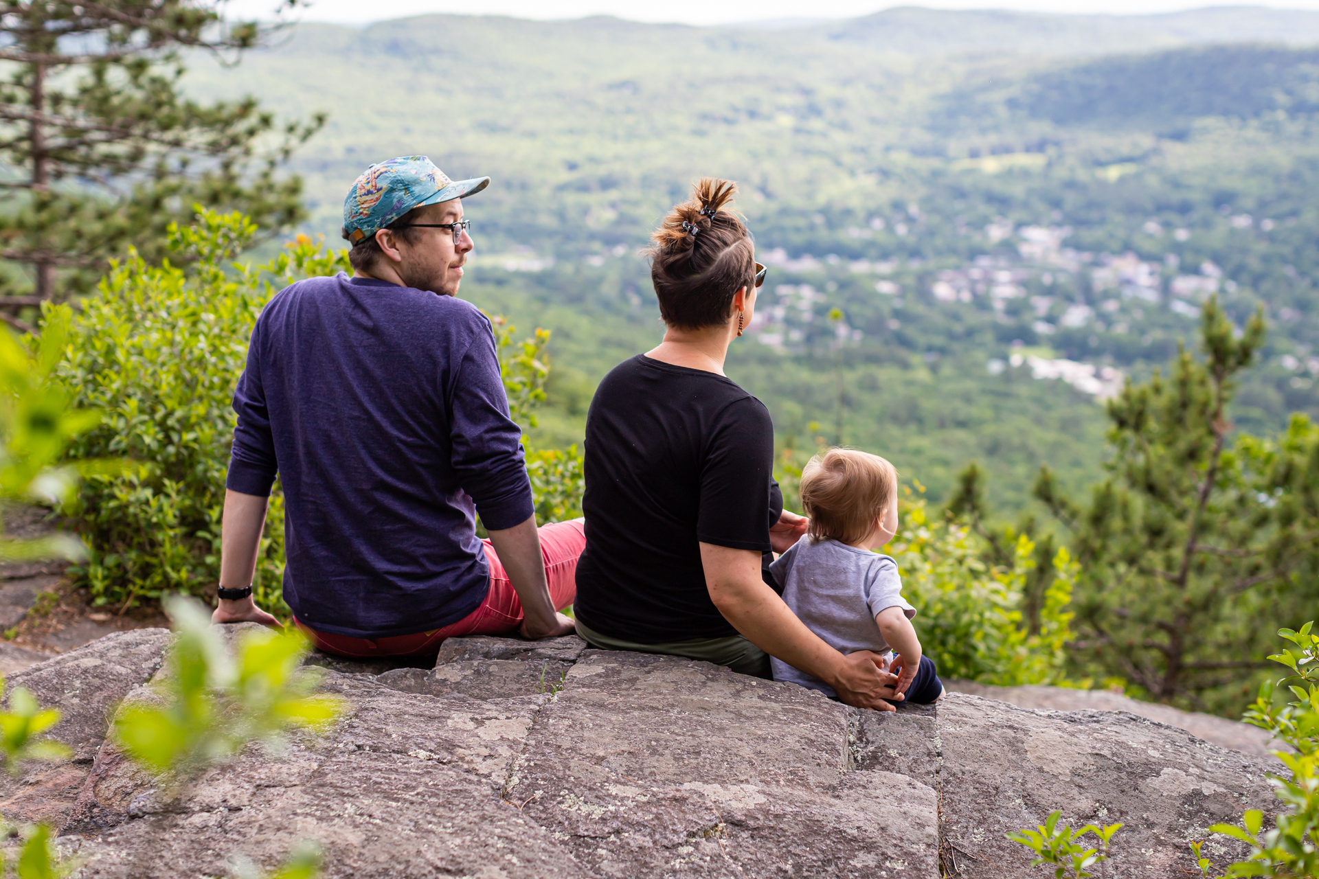 Man, woman, and toddler sitting on a rock looking out at the view