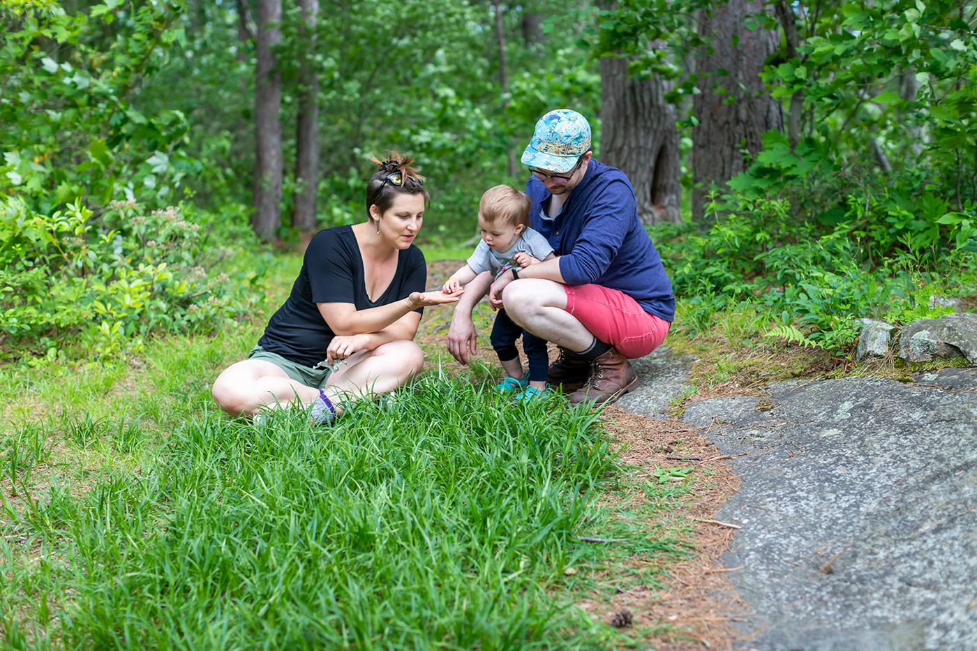 Mom, toddler, and dad looking at something found in the grass.