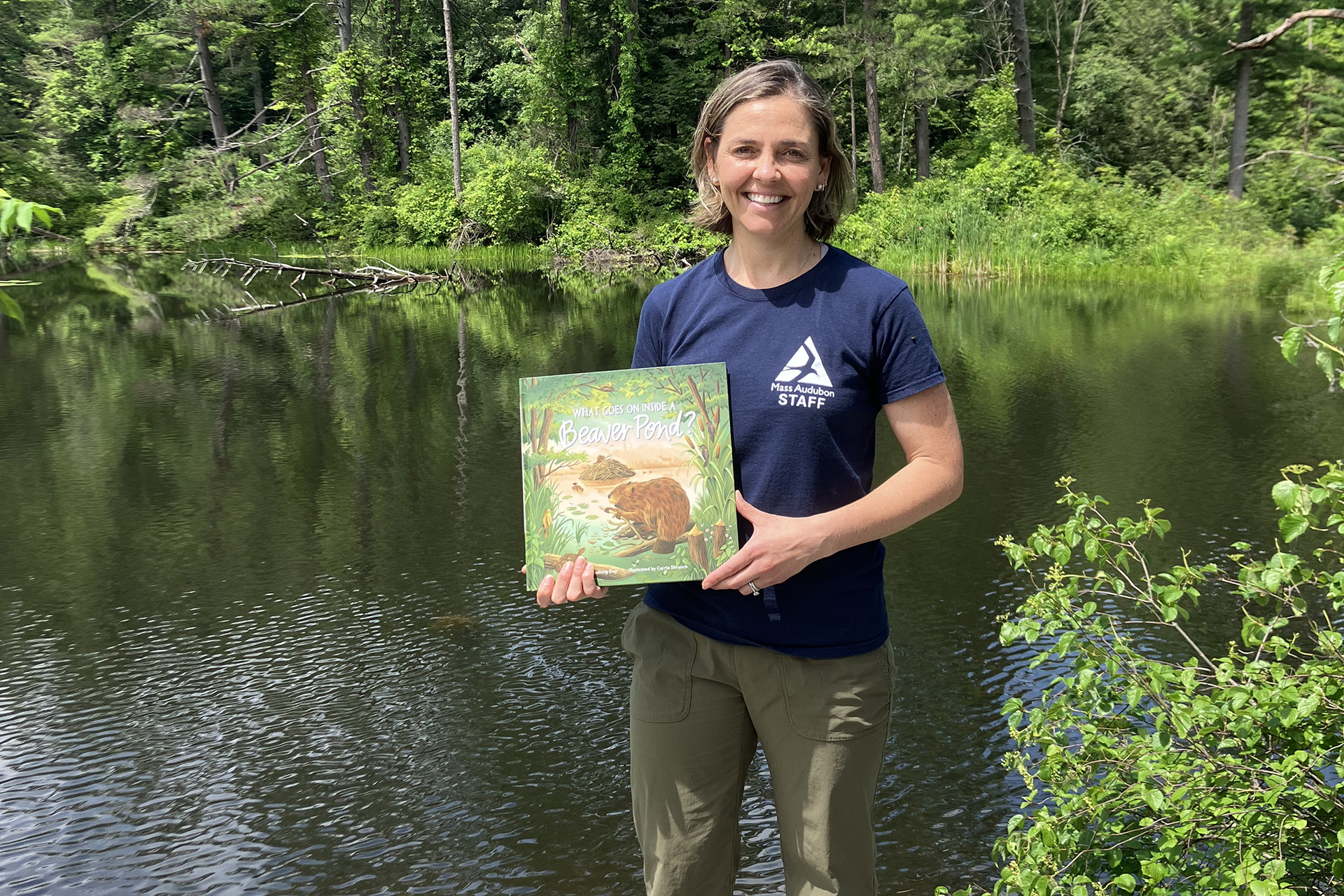 Becky Cushing Gop holding her book, posed for a photo in front of a pond