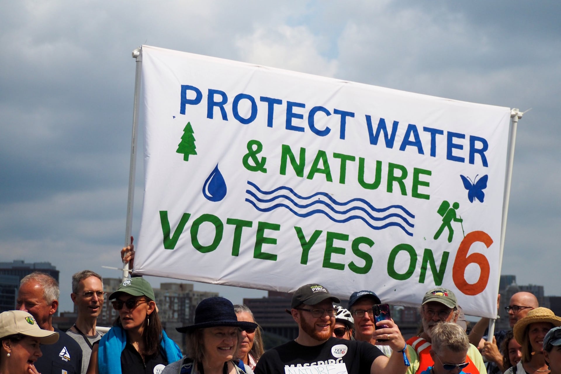 Banner that reads "Protect water & nature vote yes on 6" held above a crowd of people