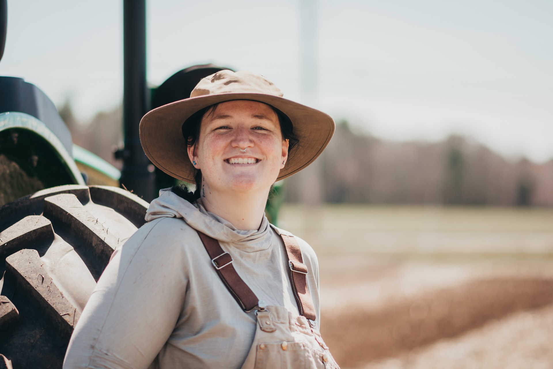 A smiling Sofia Koso, Farm Manager at Moose Hill, stands in front of a tractor in a field.