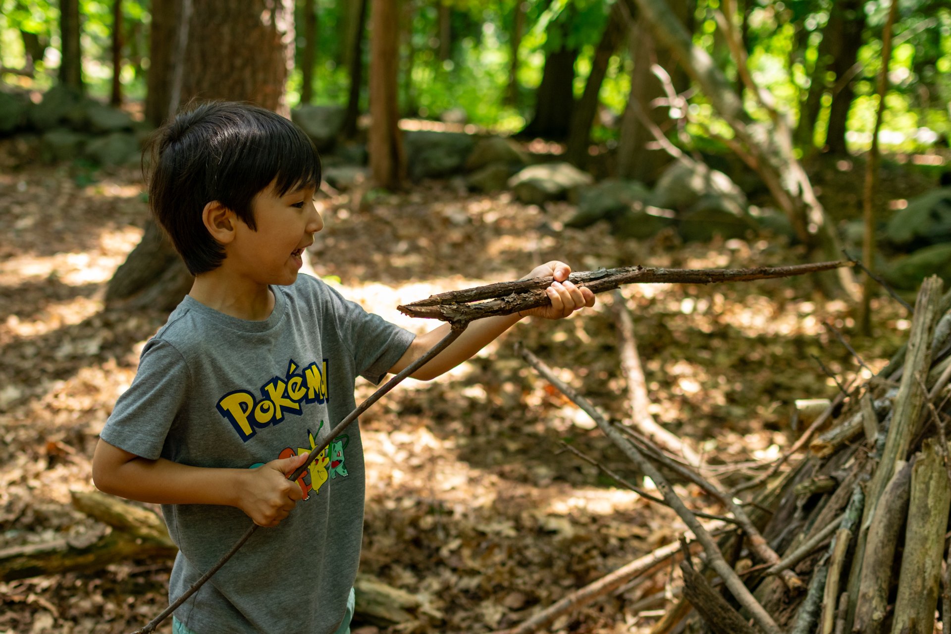 A camper at Habitat Nature Camp inspecting a branch before he adds it to his shelter in the woods