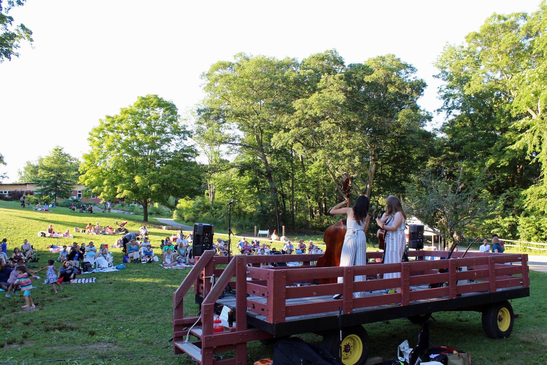 A drummer, guitarist, and singer on a wagon playing in front of people on lawn chairs and blankets on a hillside.