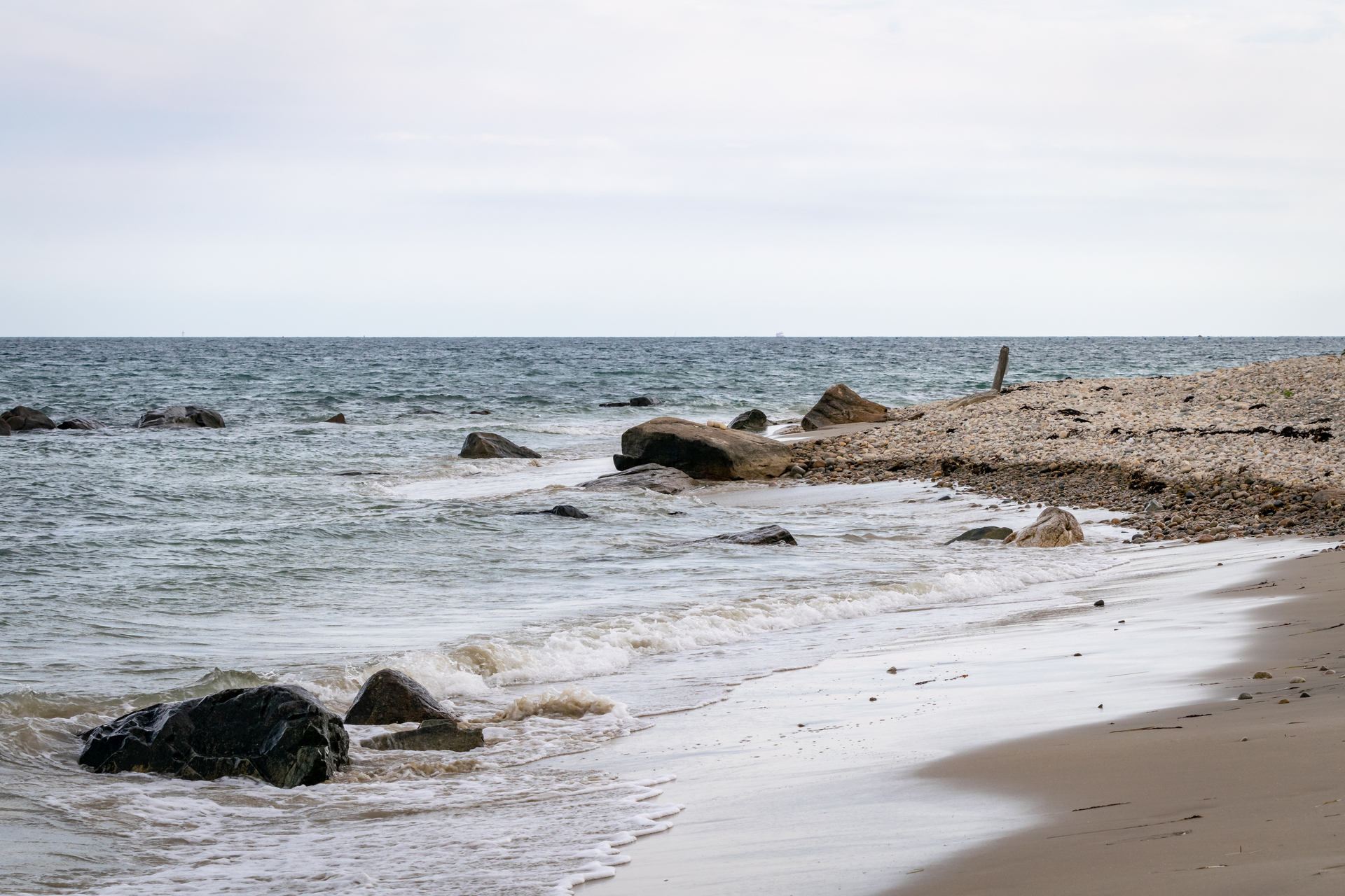 A slight rocky slope into ocean water. Large, sharp rocks stand out of the shallow water.