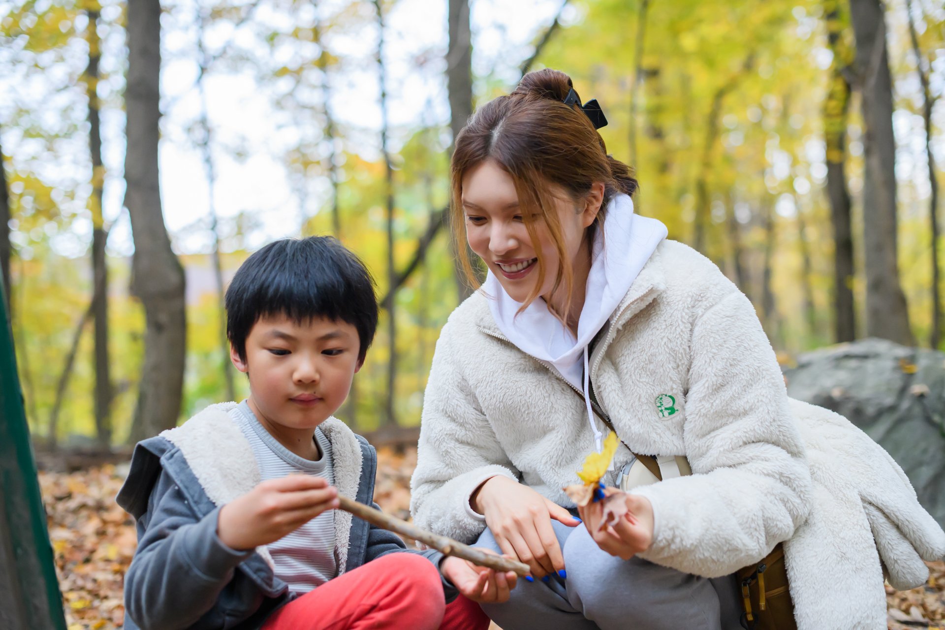 A smiling mother and son crouching on a trail at Broad Meadow Brook in Worcester, examining leaves and sticks.