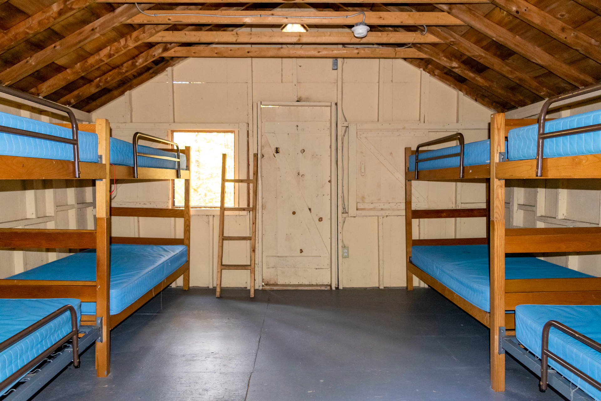 The interior of a camp cabin with wooden bunk beds and blue mattresses