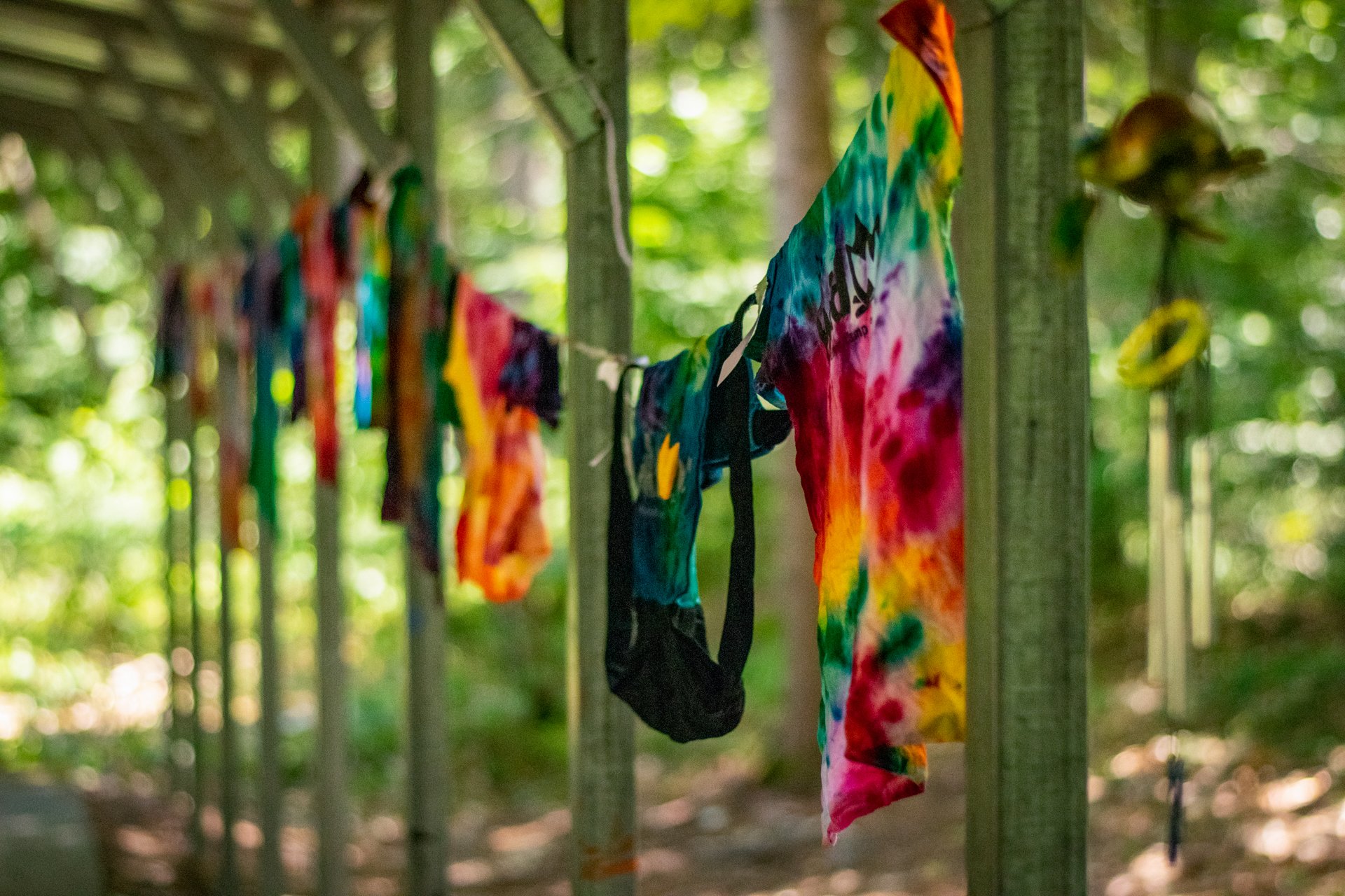A variety of freshly tie-dyed shirts hang drying on a clothesline strung between wooden posts at Wildwood's Arts & Crafts pavilion