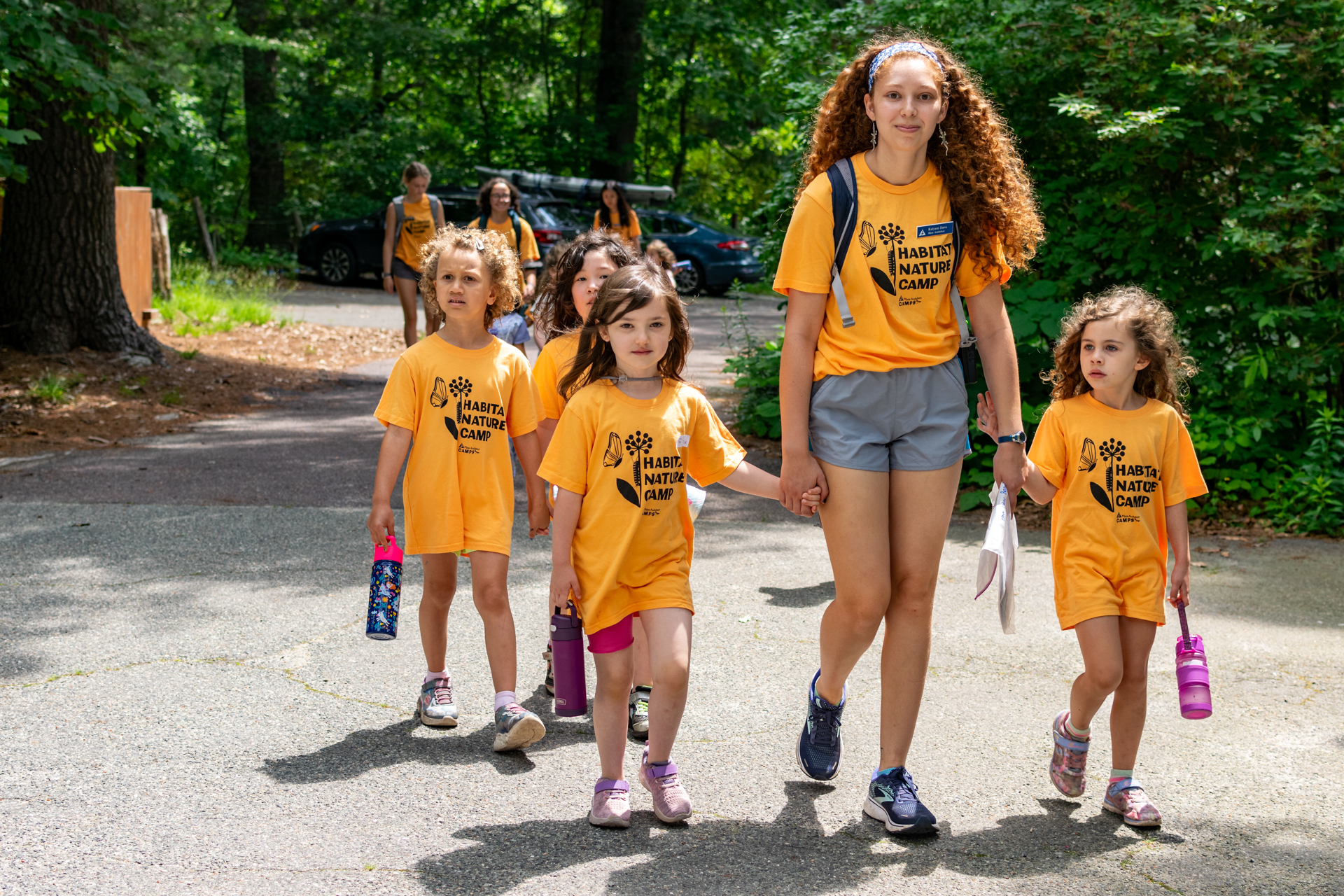 A counselor at Habitat Nature Camp walking and holding hands with two campers