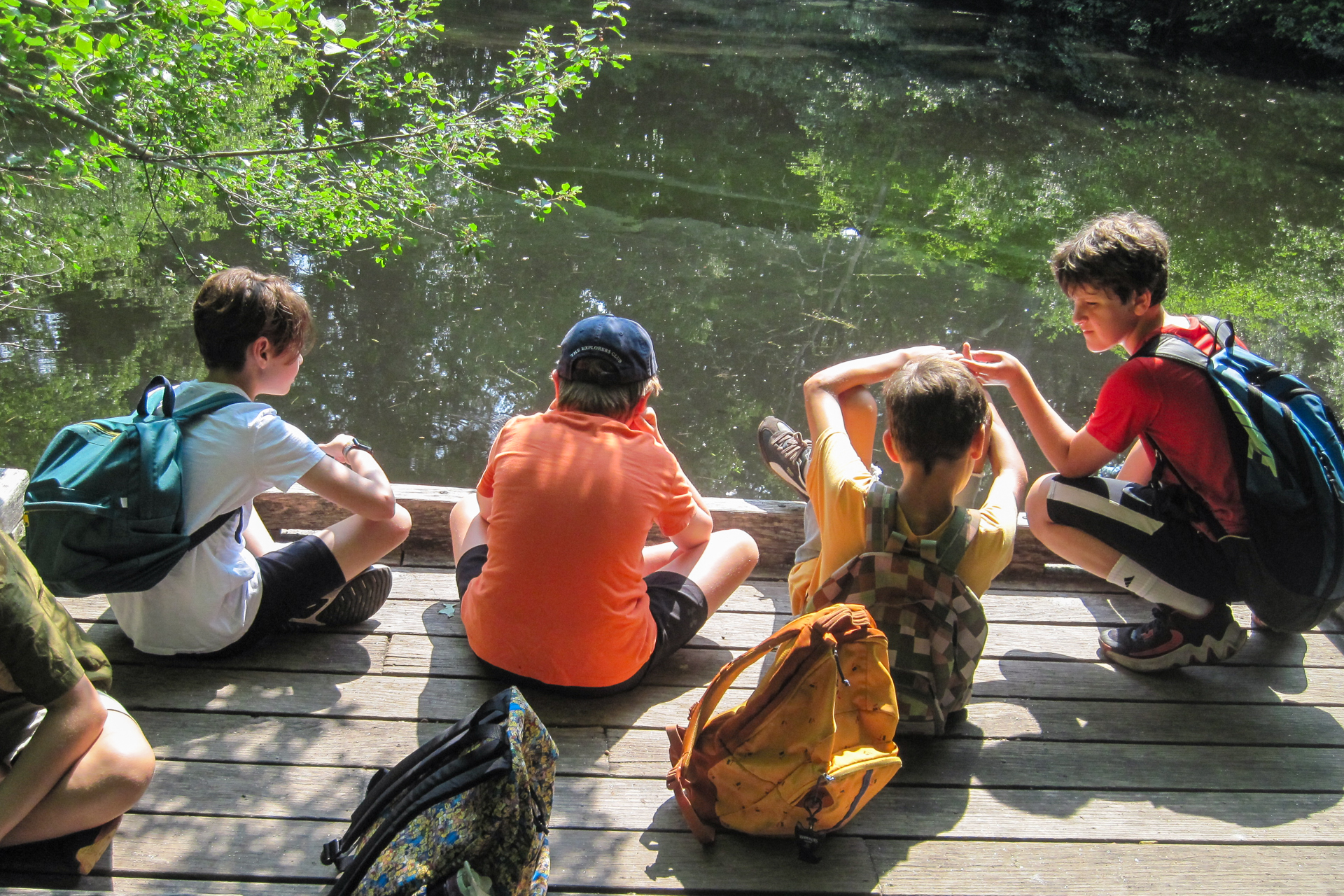 A group of campers at Habitat Nature Camp taking a break to sit at the edge of the observation deck overlooking the pond
