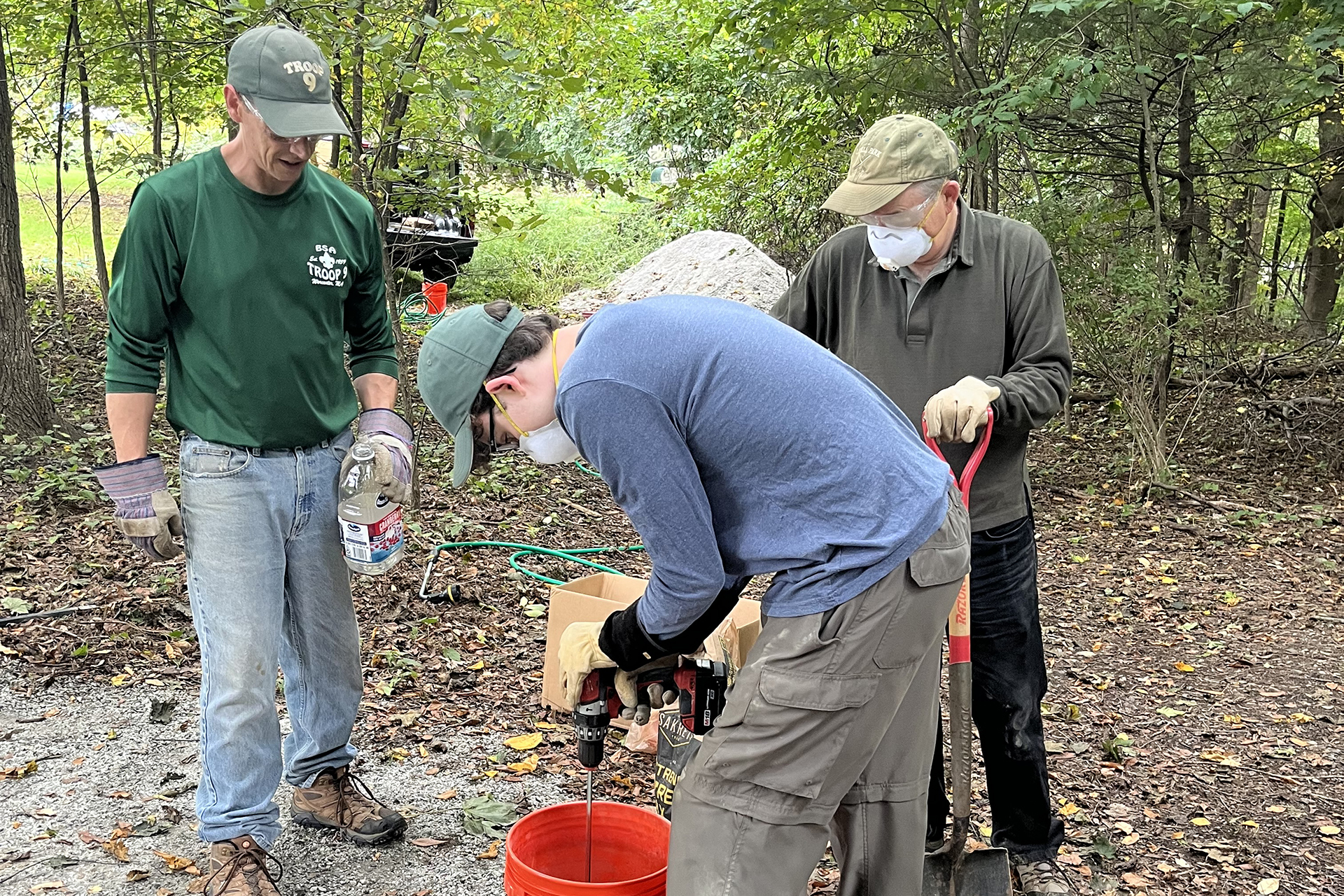 Two property managers supervise an Eagle Scout, mixing concrete to be used to anchor a bench