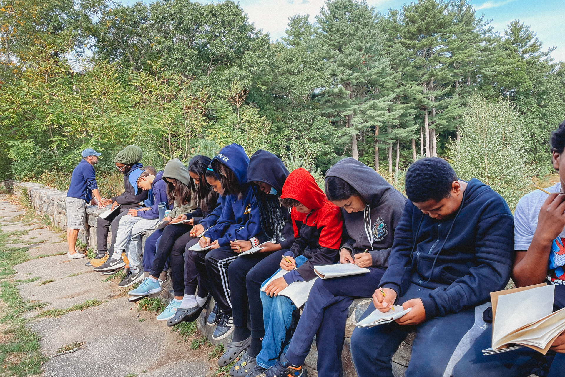 A dozen students sitting on a rock wall and writing in their journals