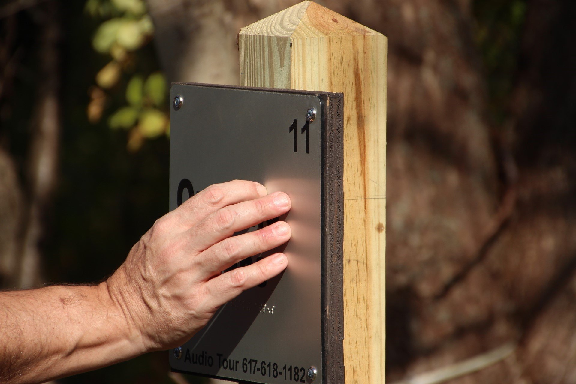 A hand reading braille on a metal sign with the number 11 on it.