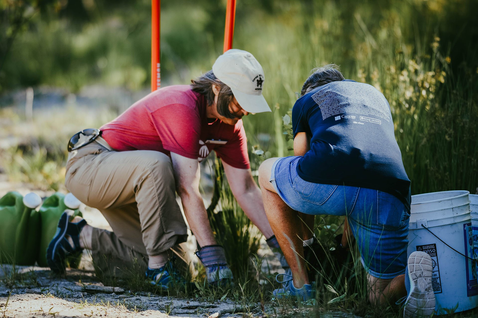 Two people, one in a red shirt and one in a blue, kneeling on the ground working in the dirt.