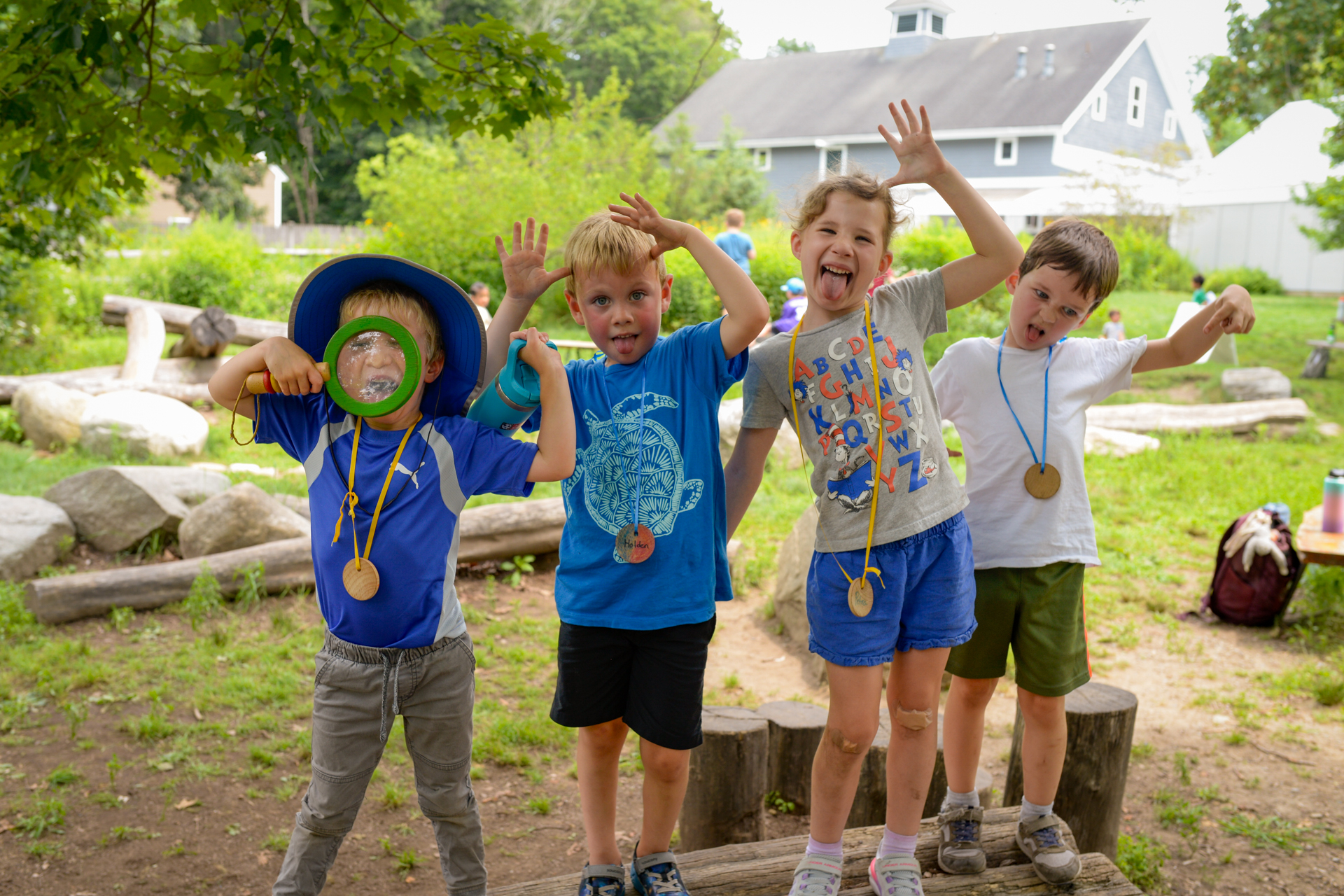 A group of four campers standing on a stump jump in the Nature Play Area making silly faces