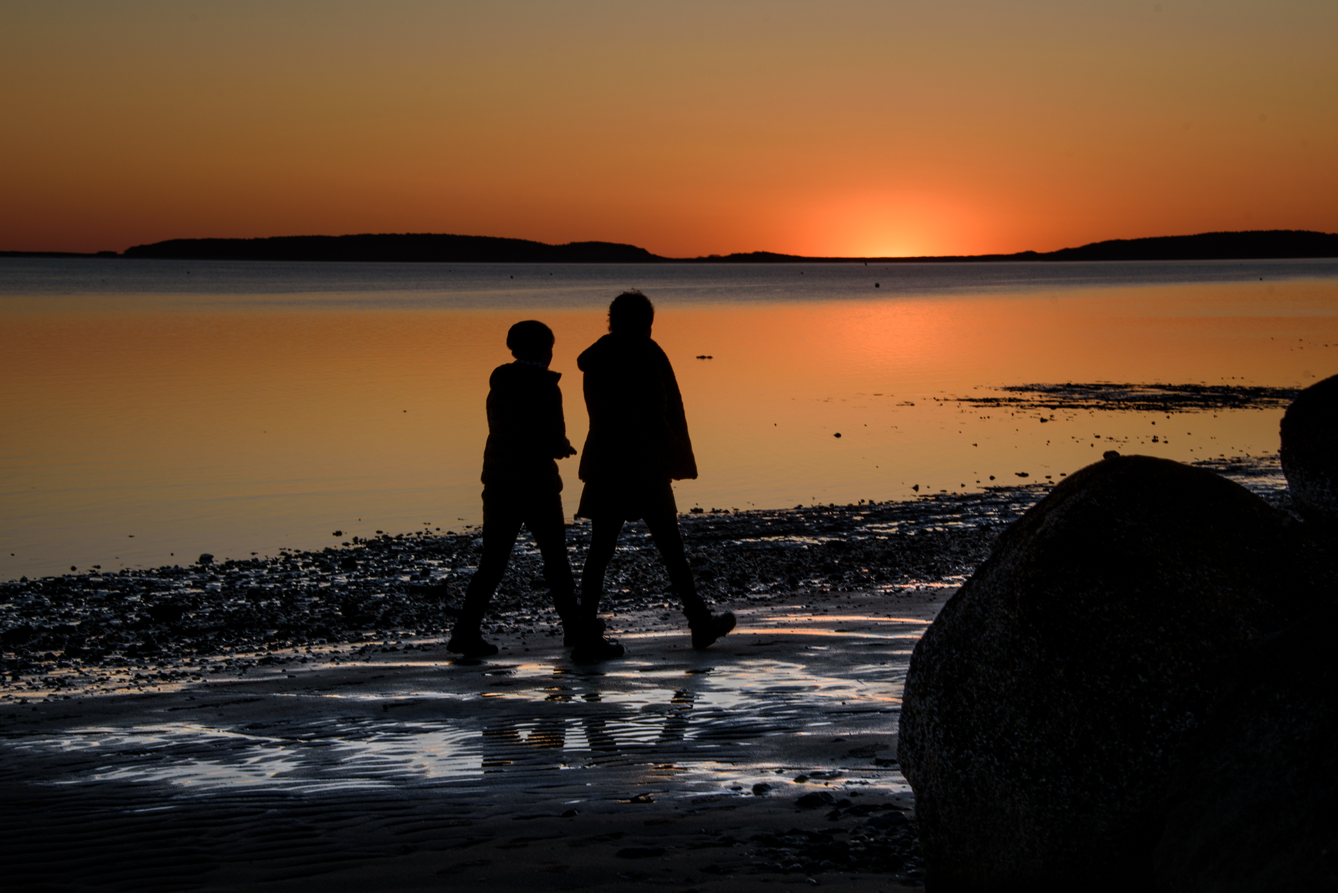 silhouetted outline of two people walking on coast at sunset