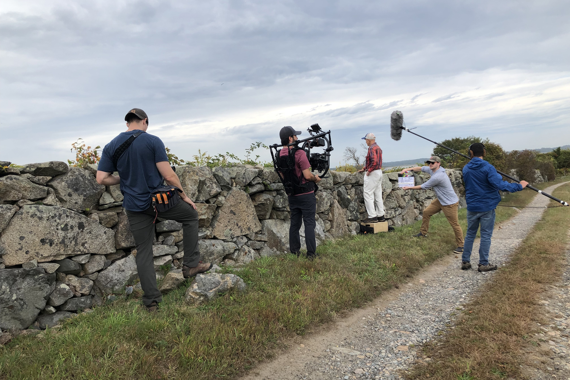 film crew filming man standing next to stone wall