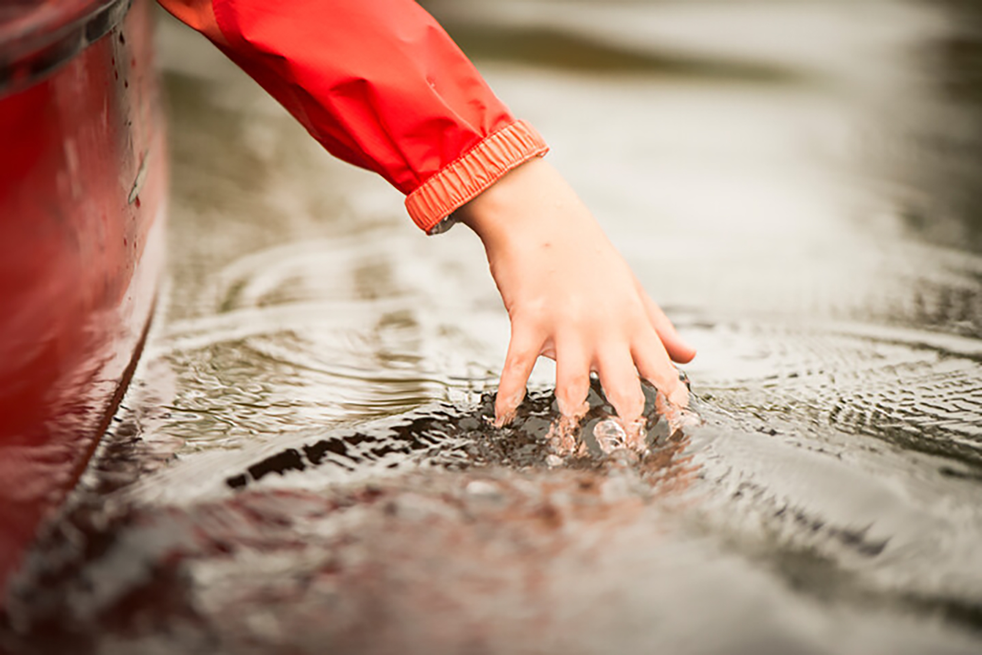 A person in a canoe skimming the water's surface with their hands
