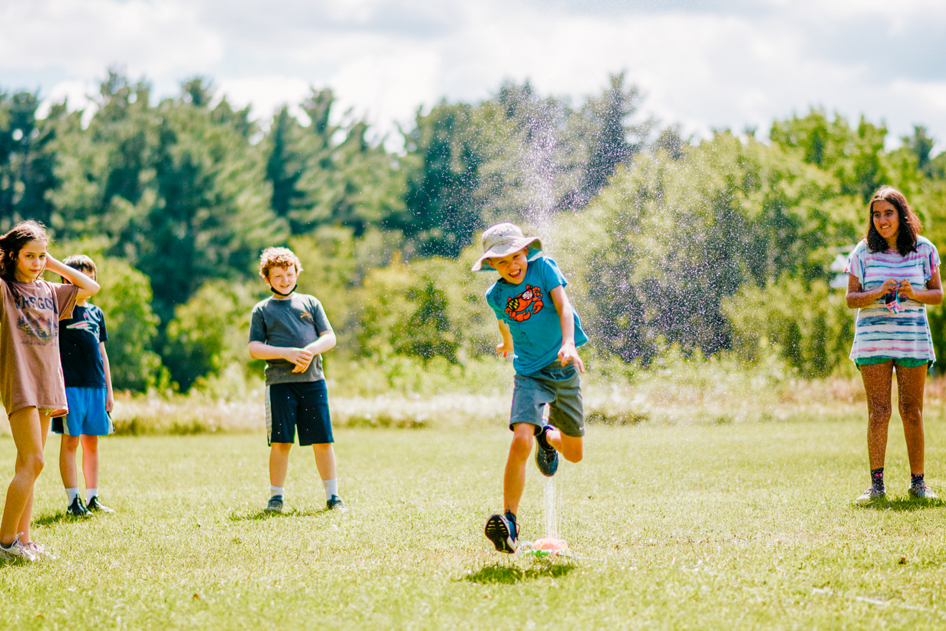 Stony Brook campers playing water games and running through a sprinkler on a hot summer day