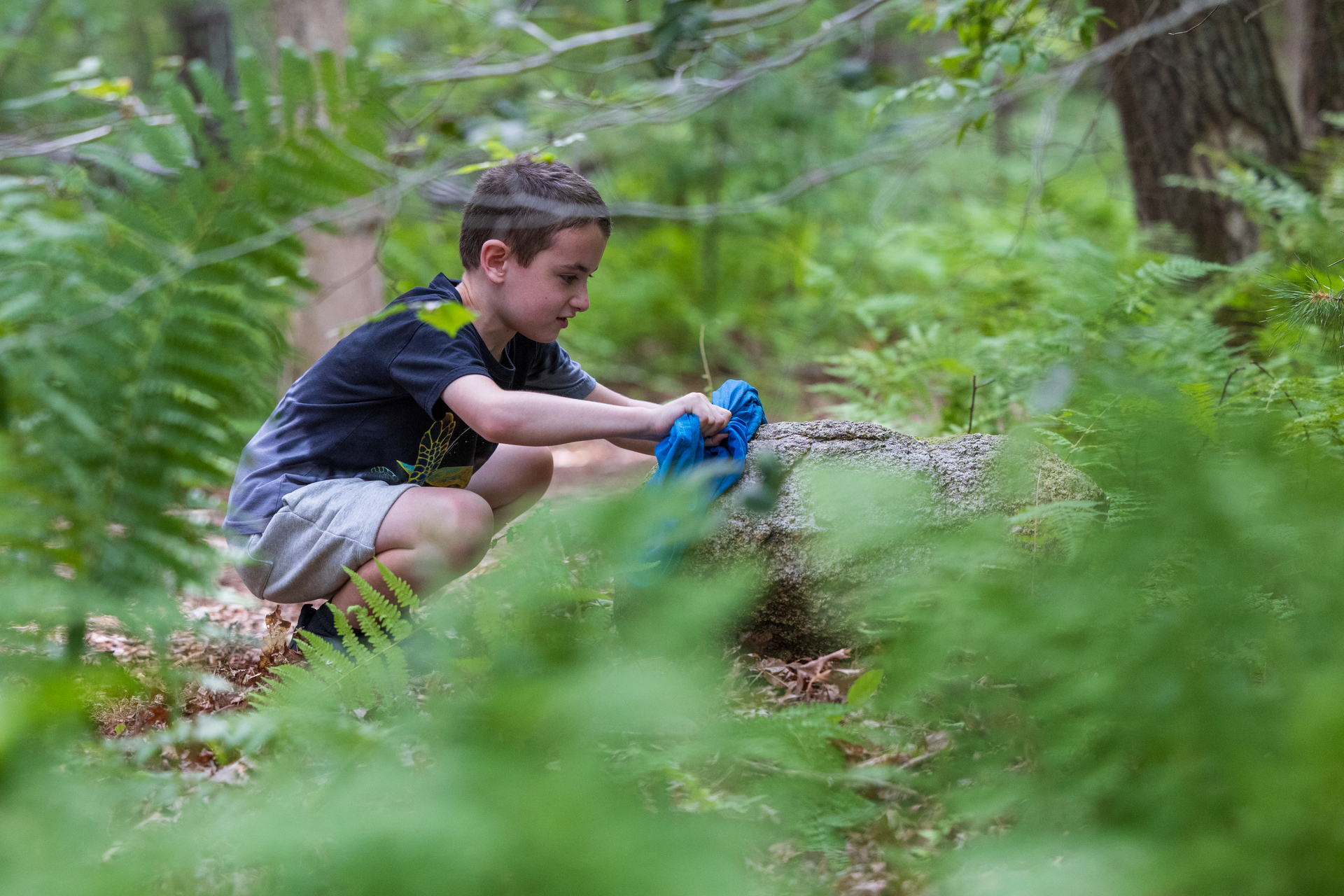 camper crouches amongst leaves and trees in the woods.