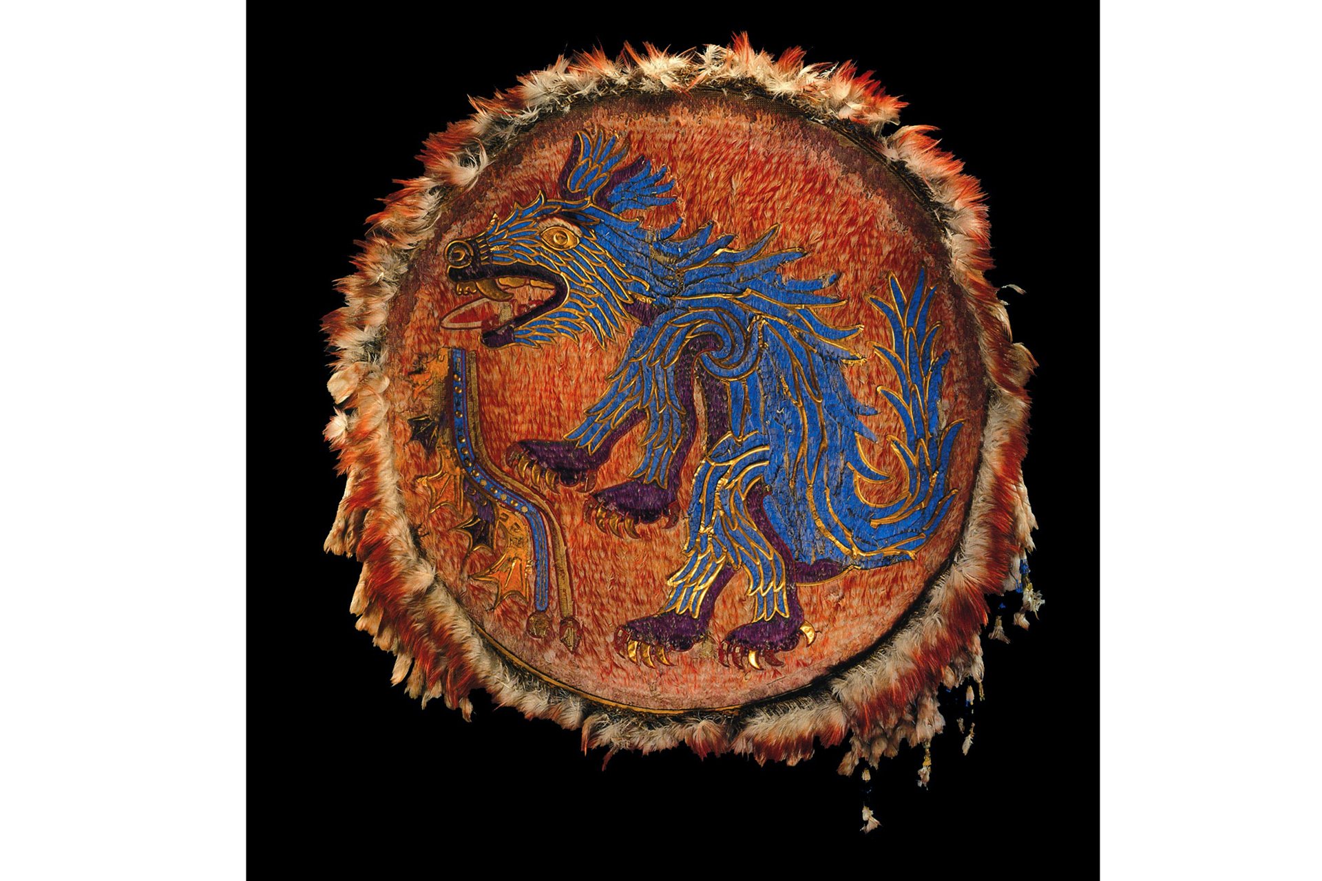 A museum display of a feather shield with a mosaic deisgn of a blue canid at its center