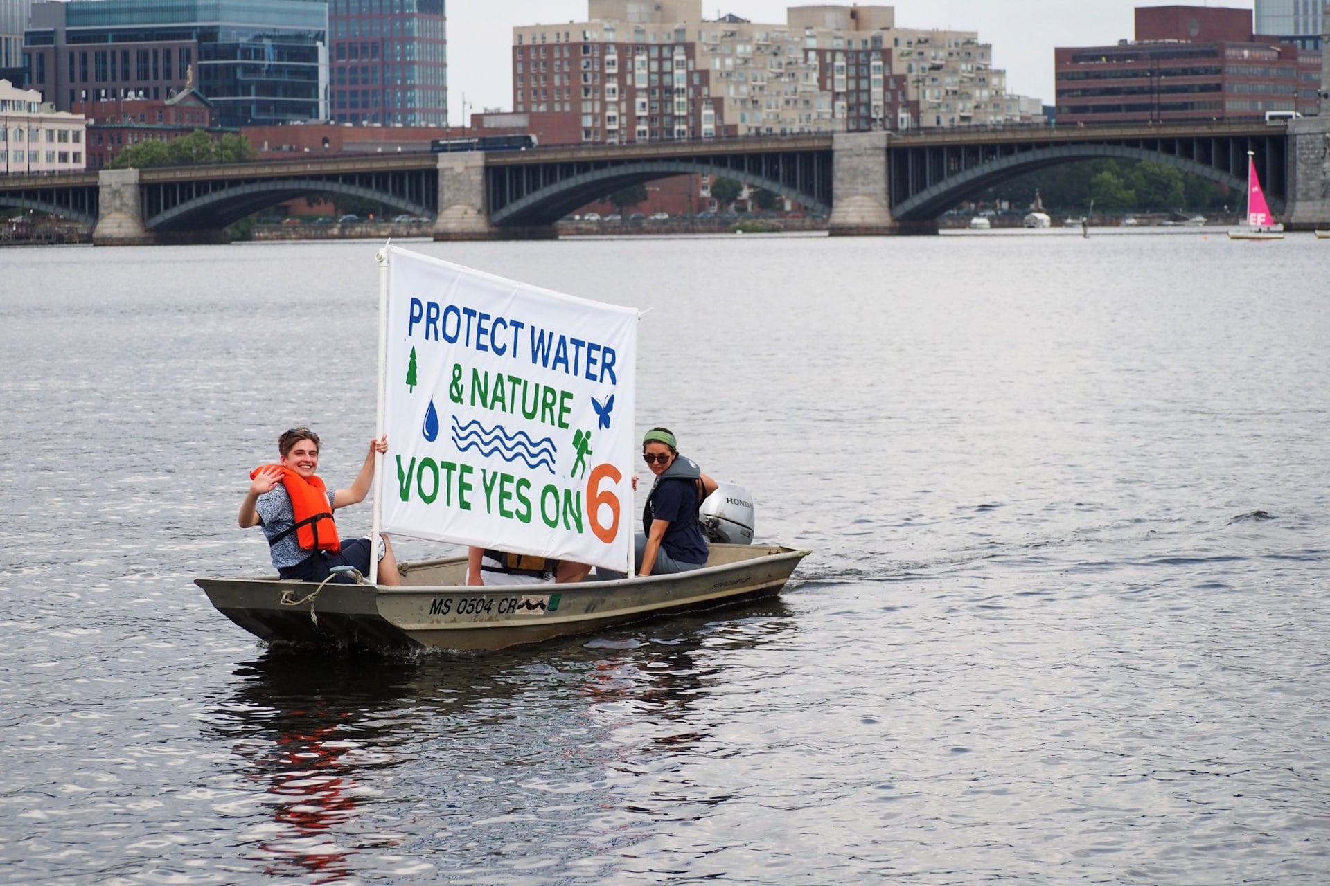 Two people on a boat with a banner that reads "Protect Water & Nature Vote Yes on 6"