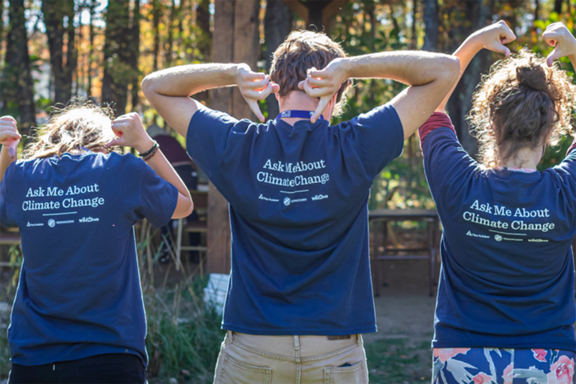 Three young adults pointing to "Ask Me About Climate Change" text written on the back of their shirts