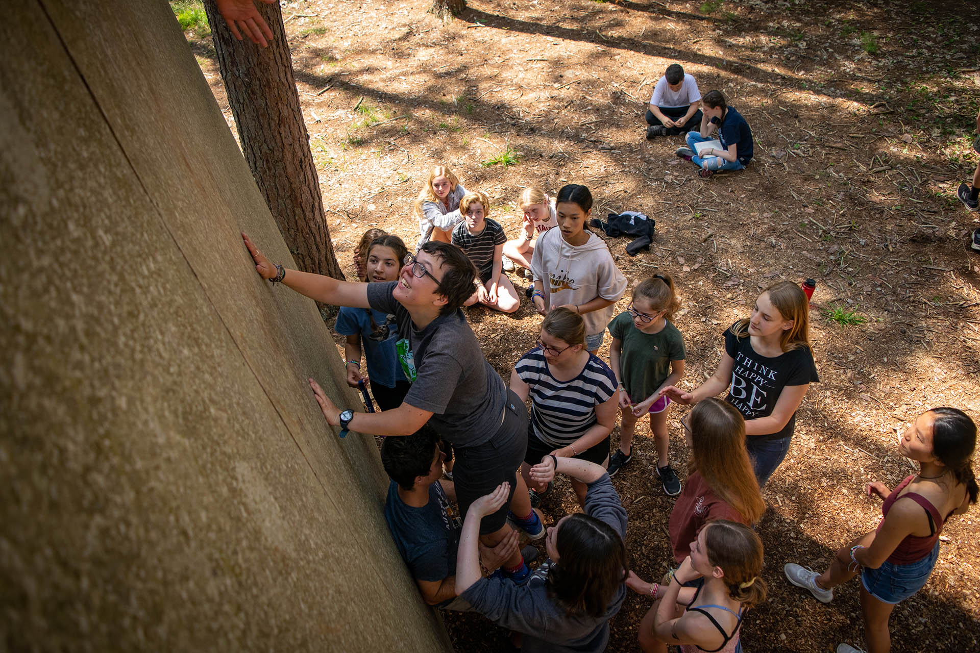 Person climbing up a wall with a group of children under her.