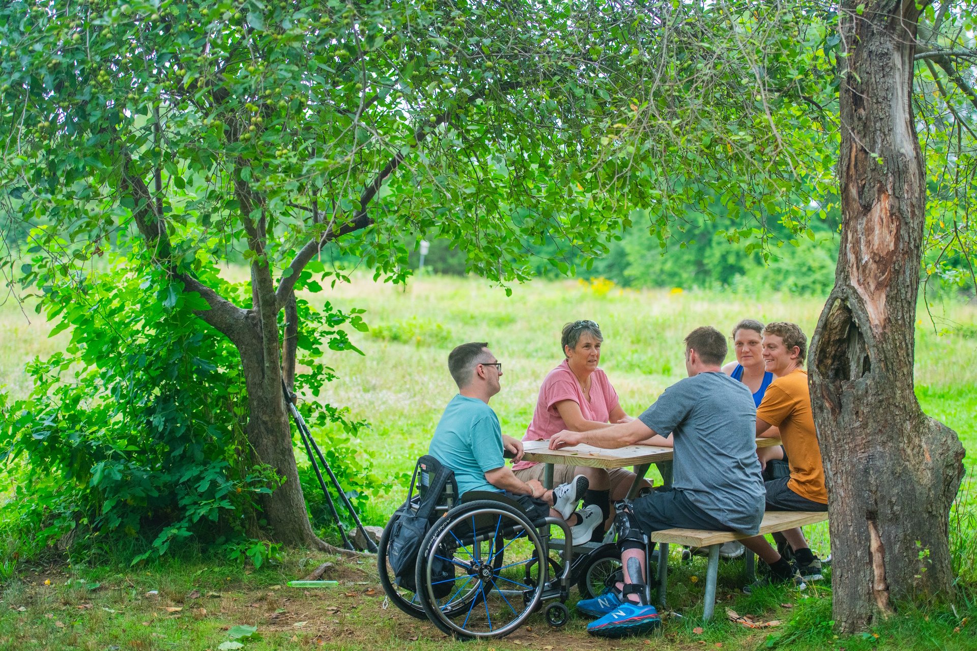 Group of five people sitting at a picnic table in the shade