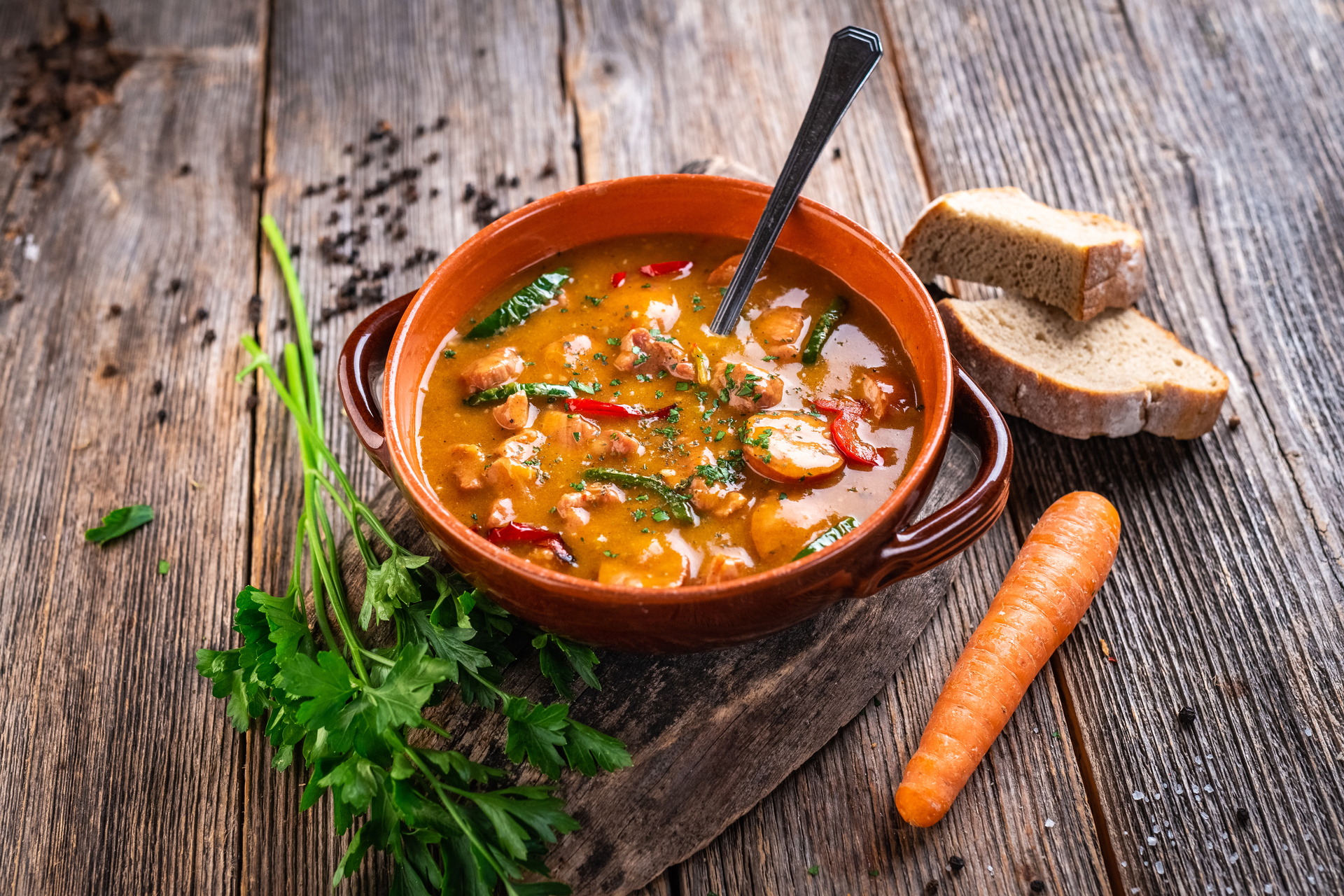 Hearty soup in an orange bowl, served with greens and bread