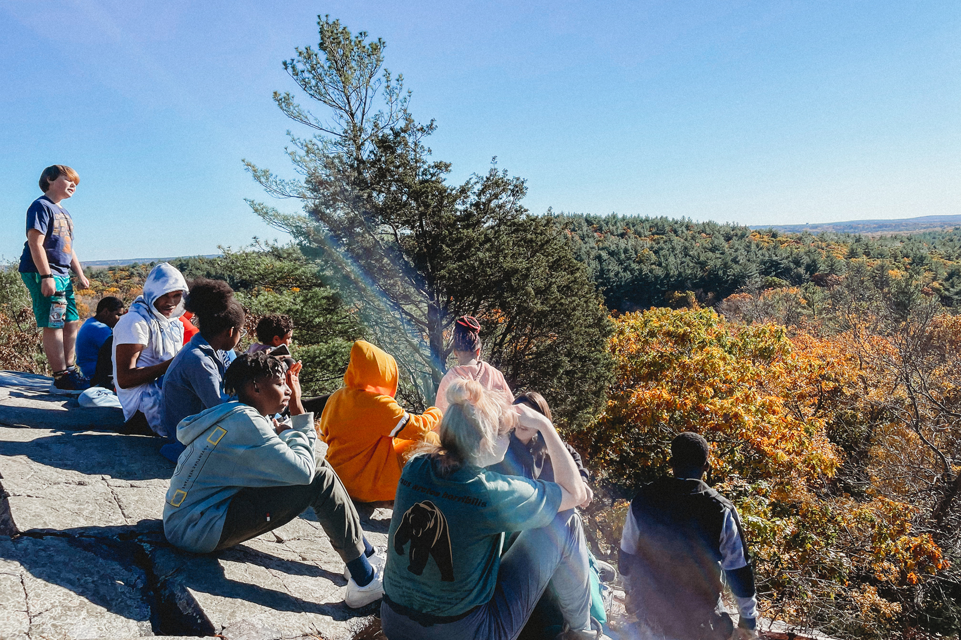 A dozen students sitting on a hill, overlooking a canopy of trees