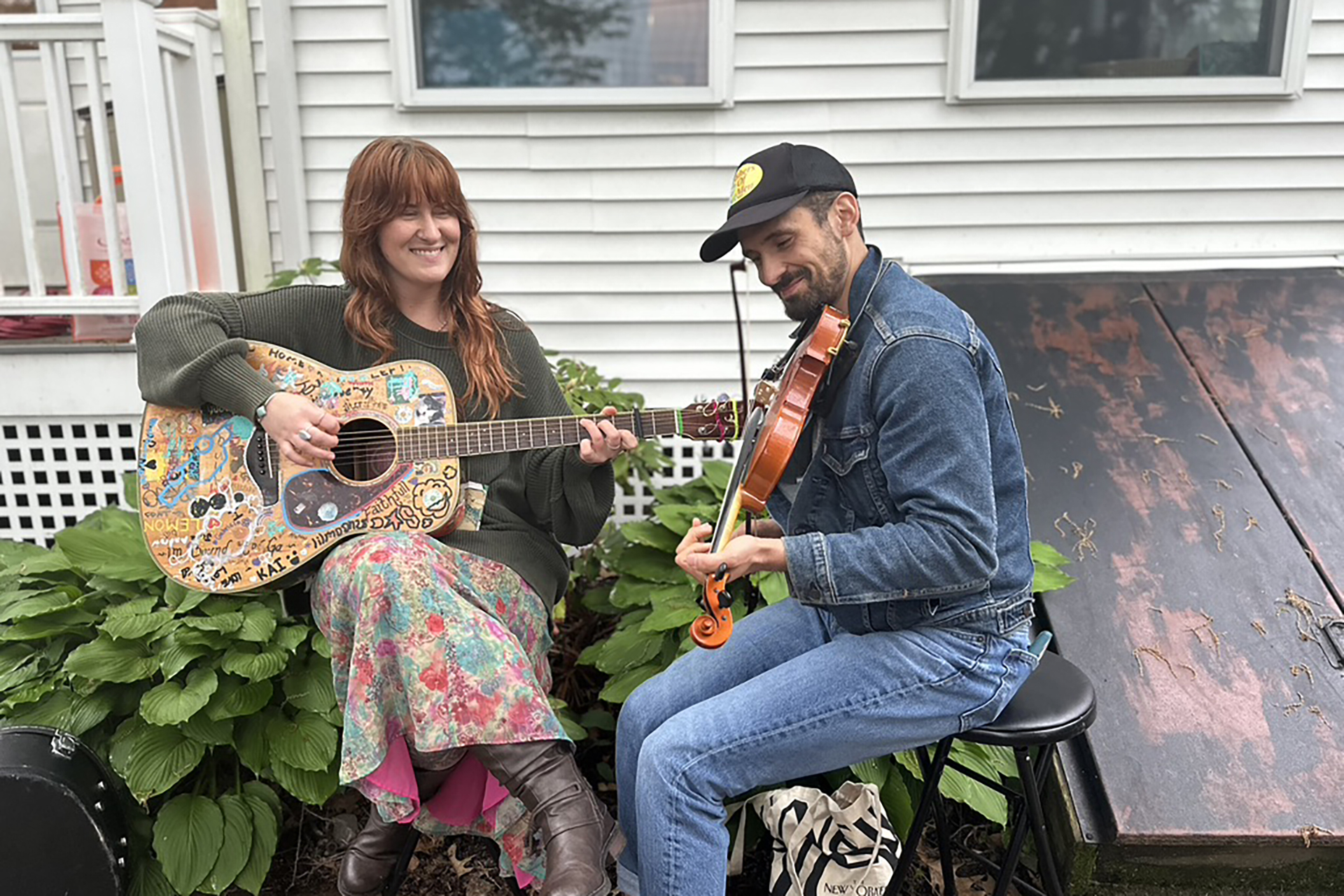 Two musicians, Nikki shattuck and Thomas Perry, sitting on stools playing a guitar and a fiddle