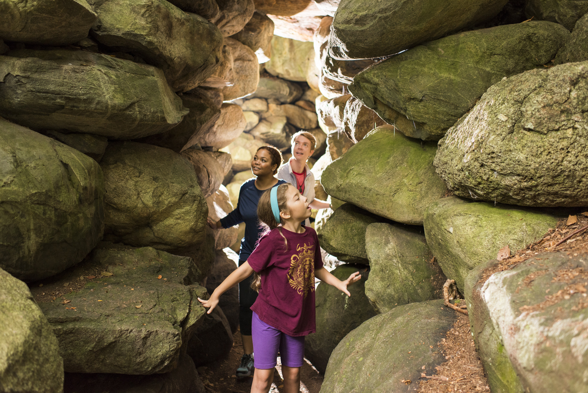 Family walking through narrow stone grotto on trail